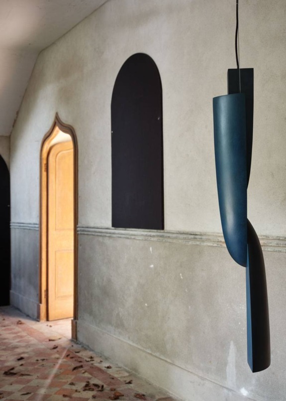 Modern blue pendant light hanging in a rustic hallway with arched doorway and stone floor.