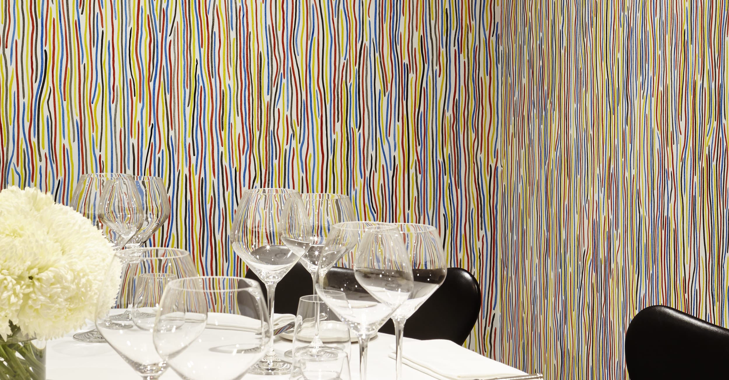 Elegant dining table set with wine glasses and white flowers, in front of a colorful striped wall background.