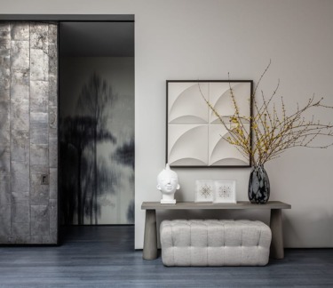 Modern interior with abstract art, a tufted bench, and a vase with branches beside a sliding metal door.
