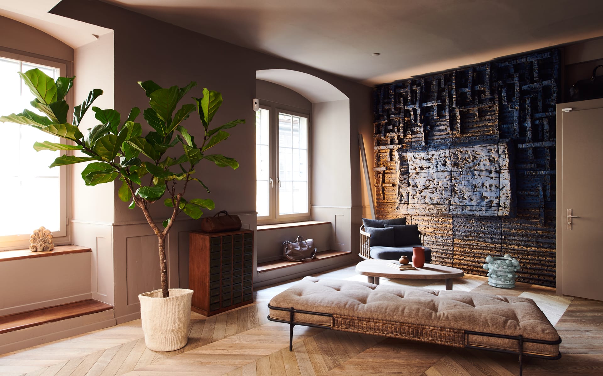 Cozy modern living room with large potted plant, cushioned bench, circular coffee table, and abstract wall art.