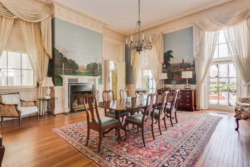Elegant dining room with wooden table, chairs, chandelier, large paintings, ornate curtains, and hardwood floors.