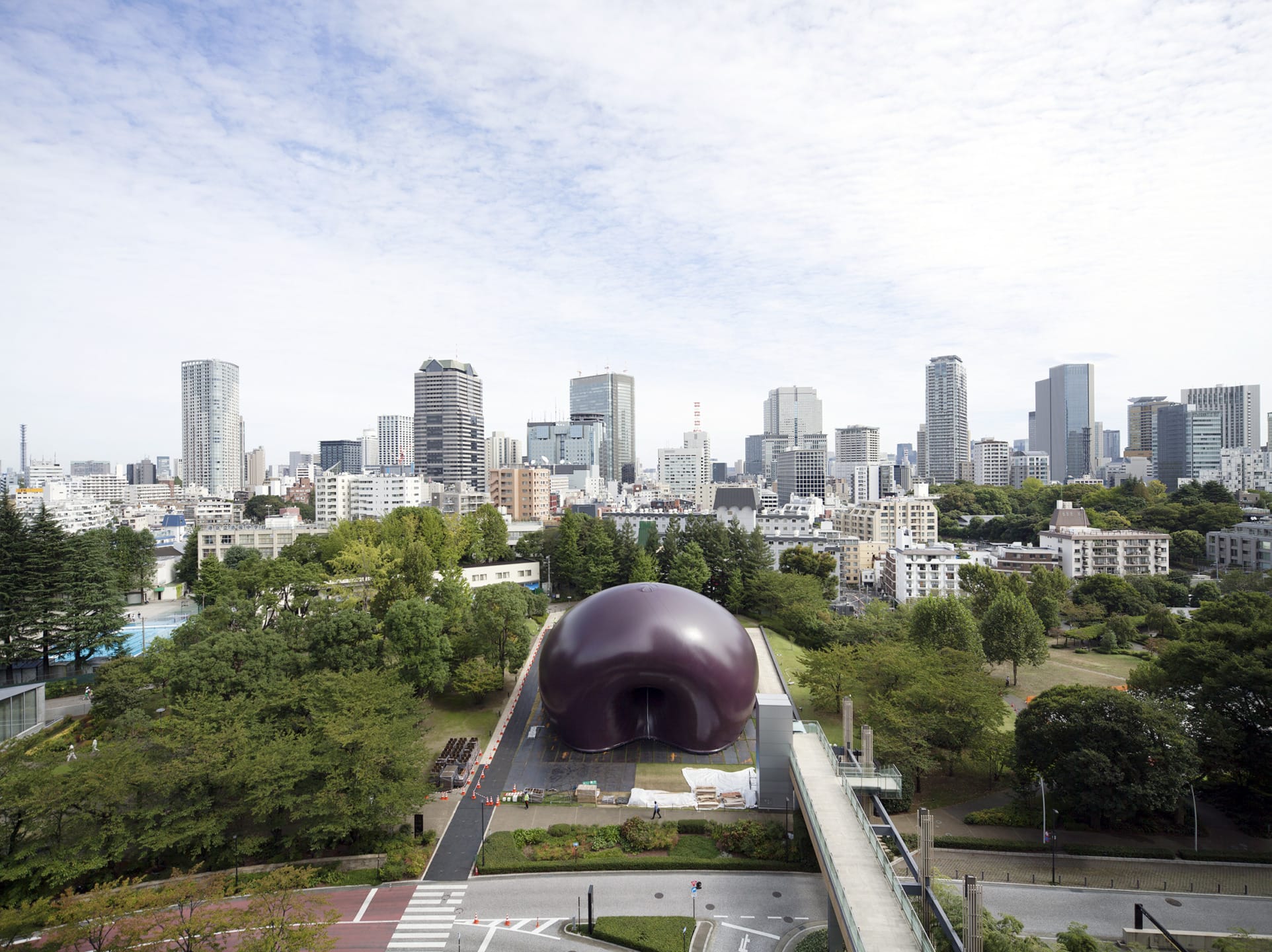 Aerial view of the Tokyo cityscape with a unique spherical structure surrounded by greenery in the foreground.