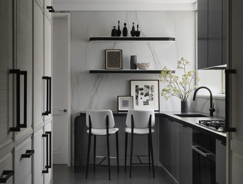 Modern kitchen with marble walls, two chairs at a counter, floating shelves with decor, and a vase with flowers.