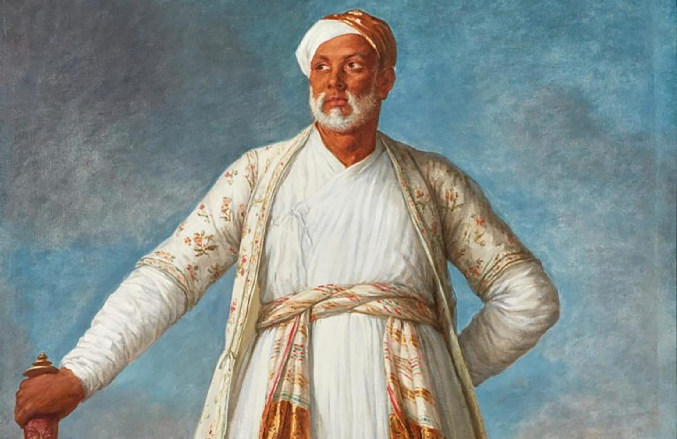 Painting of a man in traditional Indian attire, with a turban and a sword, standing confidently against a blue background.