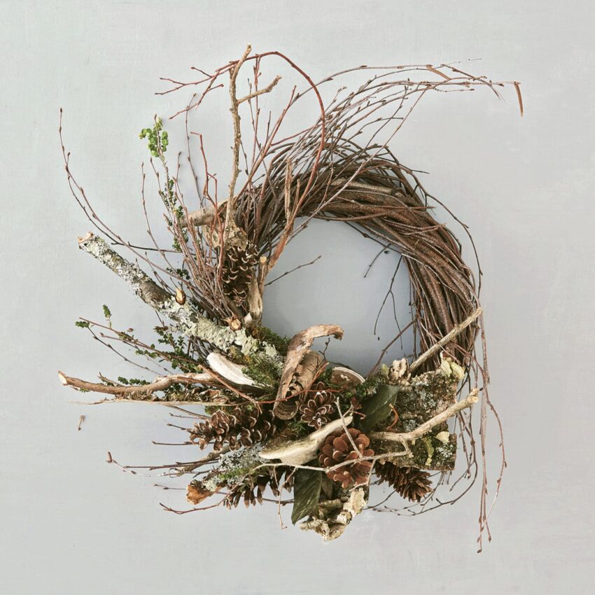 Rustic wreath made of twigs, branches, and pinecones on a gray background.