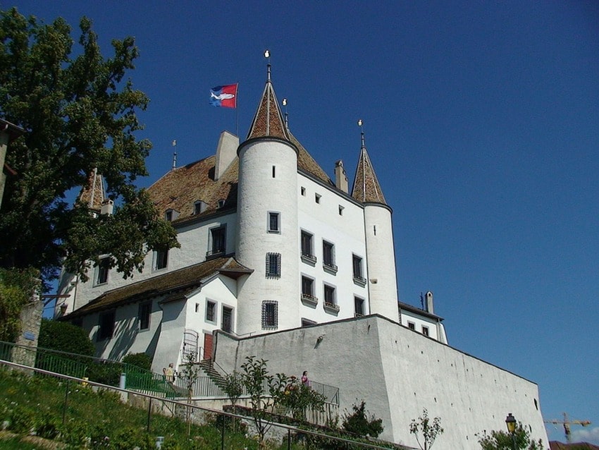 Historic white castle with multiple towers and a red and blue flag on top, set against a clear blue sky.