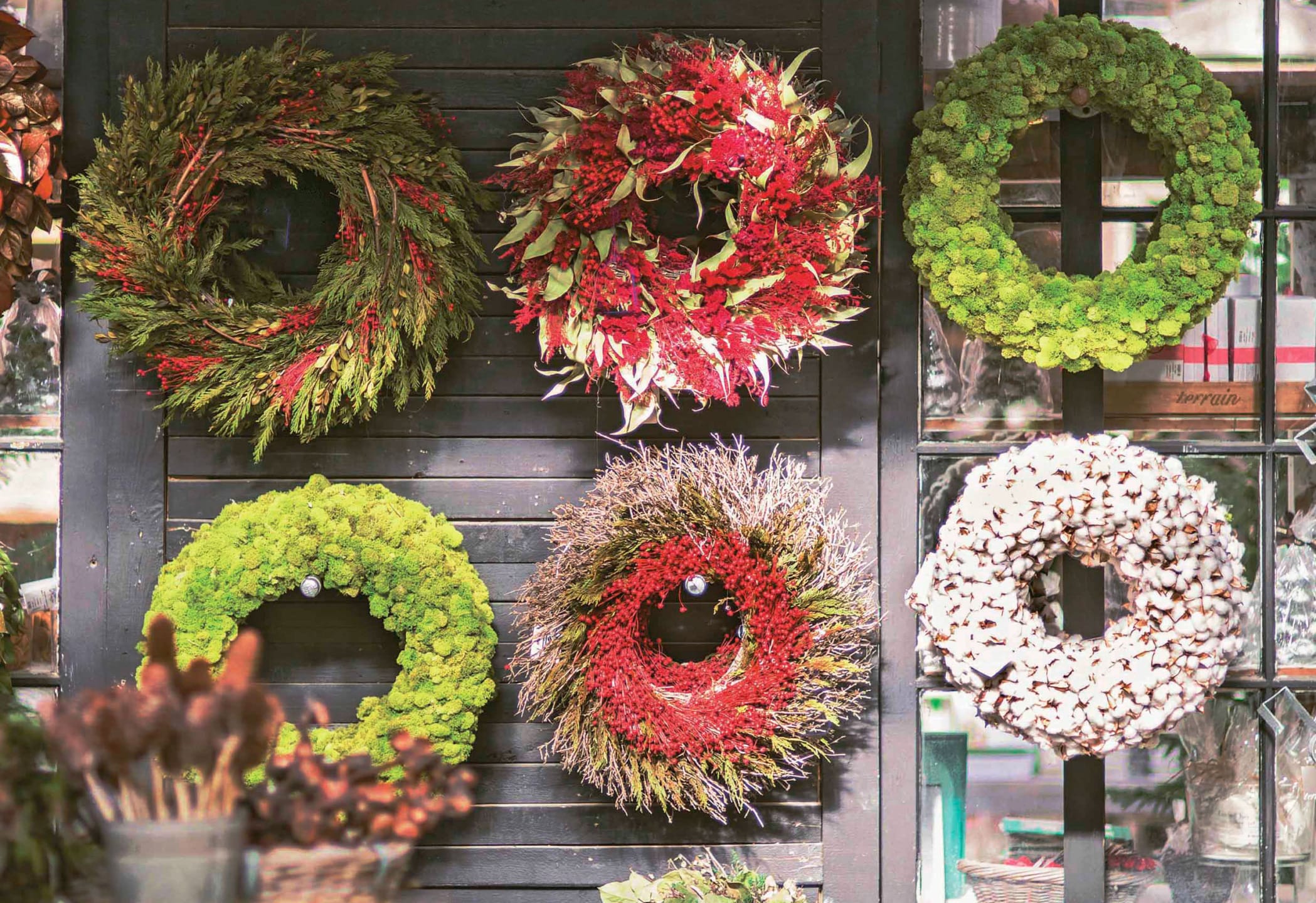 Various decorative wreaths on display, showcasing vibrant greens, reds, and browns in a bright outdoor setting.