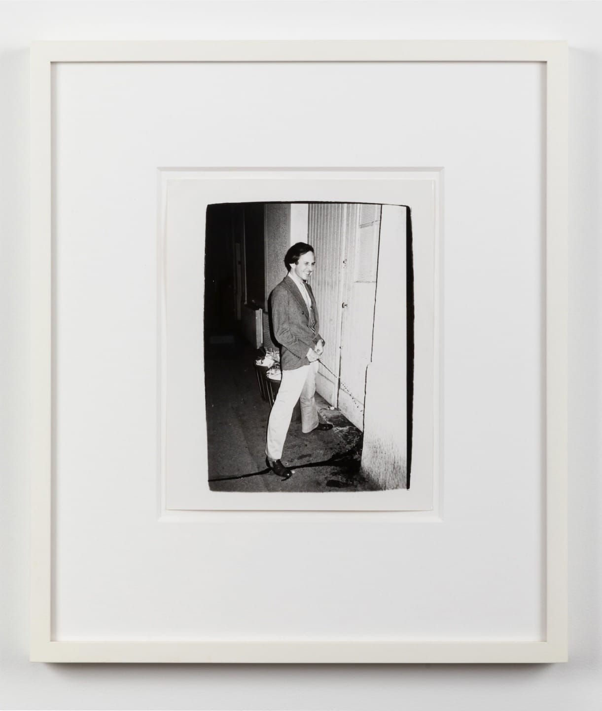 A black and white framed photo of a person standing next to a wall outside at night.