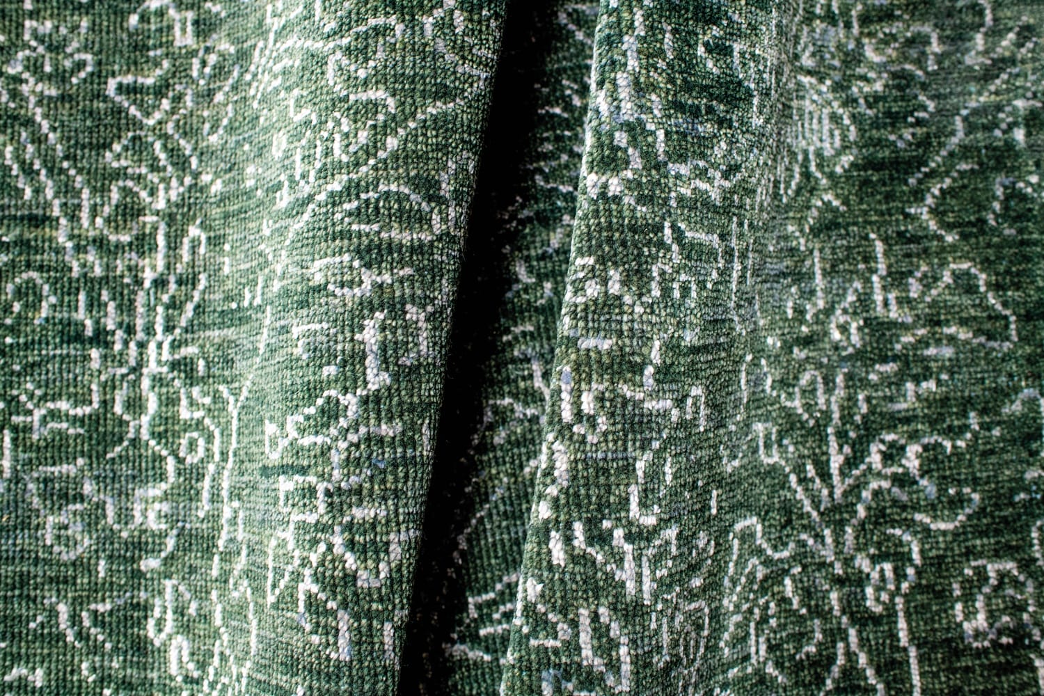 Close-up of textured green fabric with intricate white patterns and folds.