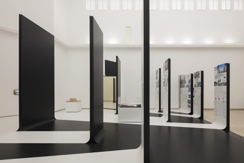 Modern art gallery installation with large black panels and informational displays in a spacious, white-walled room.