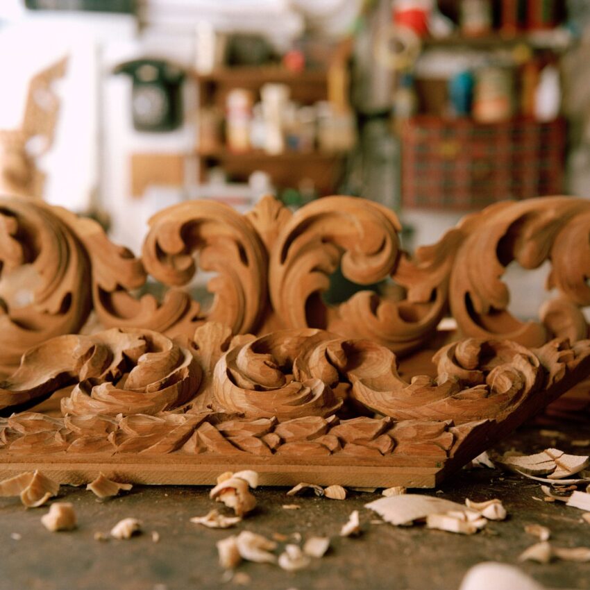 Ornately carved wooden pieces on a workshop table, surrounded by wood shavings and tools in the background.