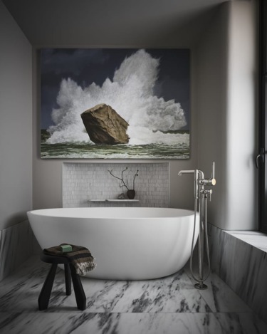 Minimalist bathroom with freestanding tub, marble flooring, and a large wave painting on the wall.