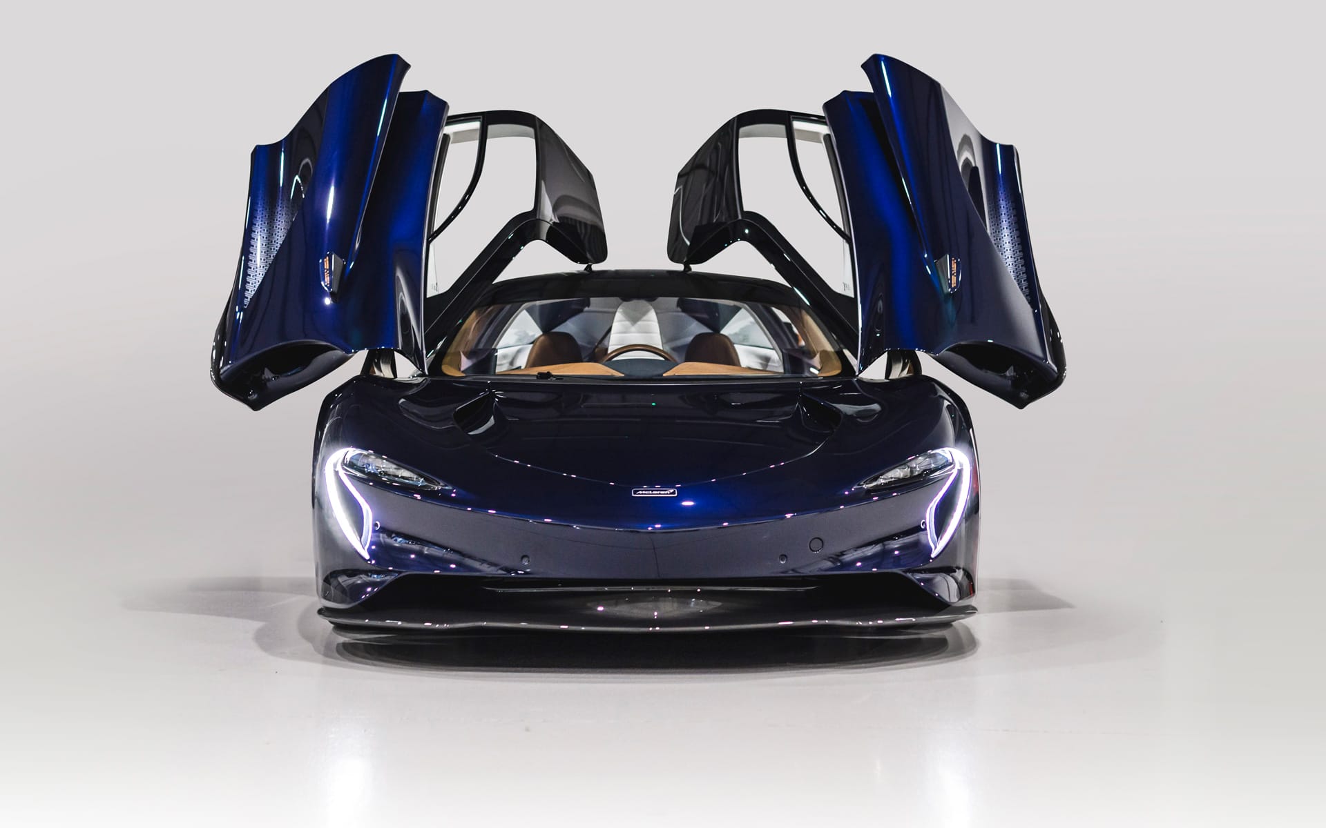 Sleek blue sports car with its gullwing doors open, showcased in a well-lit studio setting.