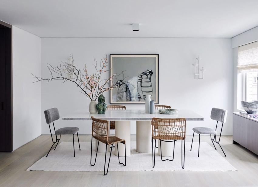 Modern dining room with white table, six mixed chairs, abstract artwork, vase with branches, and large window.