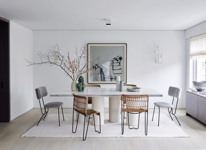 Modern dining room with white table, six mixed chairs, abstract artwork, vase with branches, and large window.