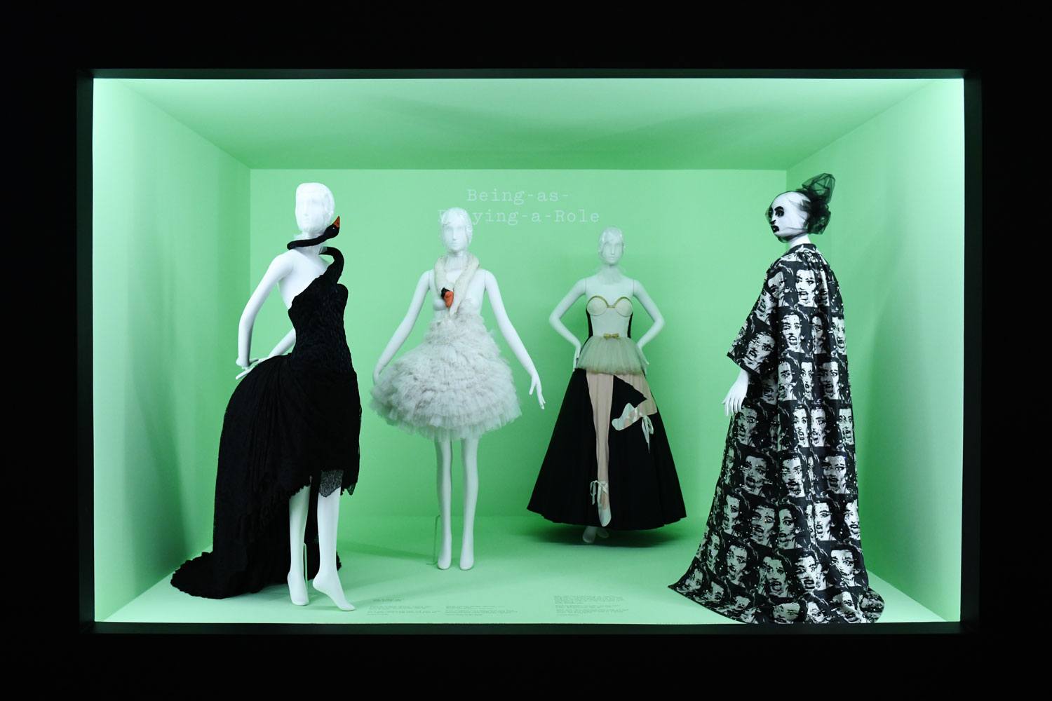 Fashion exhibit with four mannequins in unique dresses against a green backdrop, showcasing creative design styles.