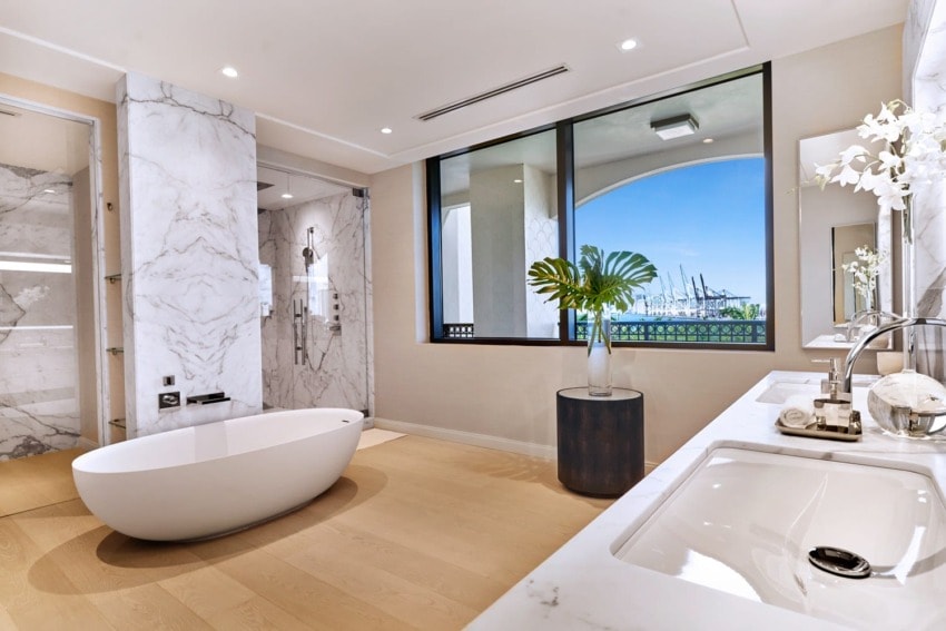 Luxurious bathroom with marble walls, freestanding tub, double sink, large window with a view, and elegant decor.