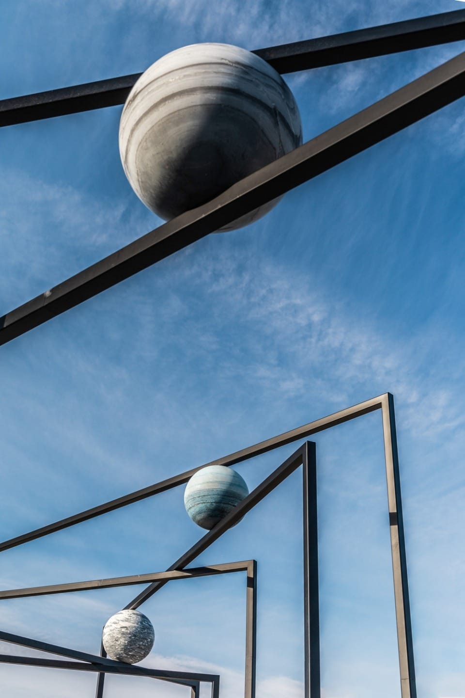 Modern art installation featuring geometric metal frames with planet-like spheres under a clear blue sky.