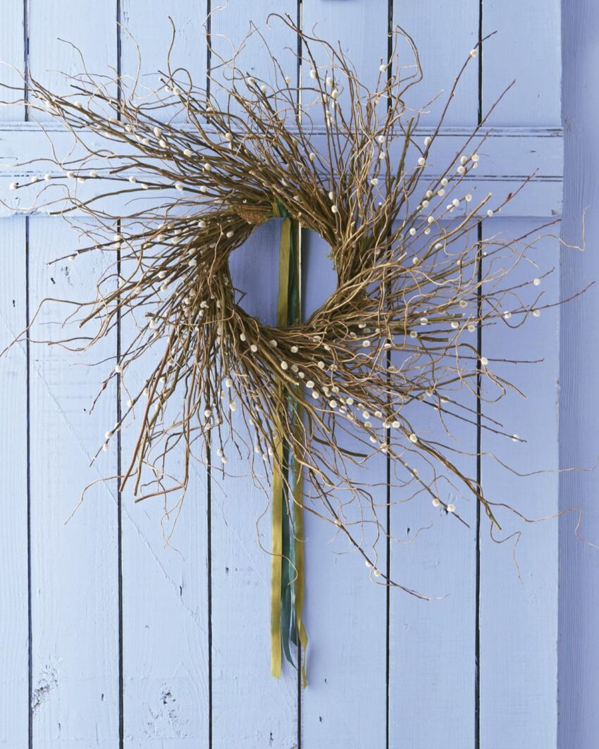 Rustic twig wreath with small white accents hanging on a light blue wooden door.