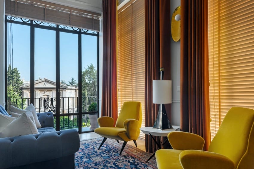 Bright living room with yellow chairs, a blue sofa, and large windows showing an outdoor view.