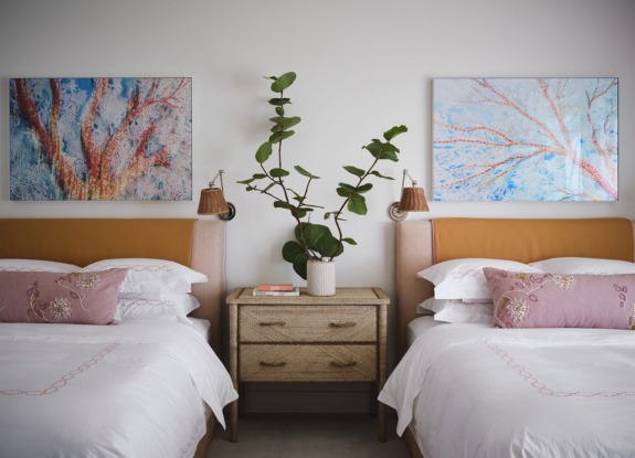 Bedroom with two beds, decorative pillows, wall art, and a leafy plant on a wooden nightstand.