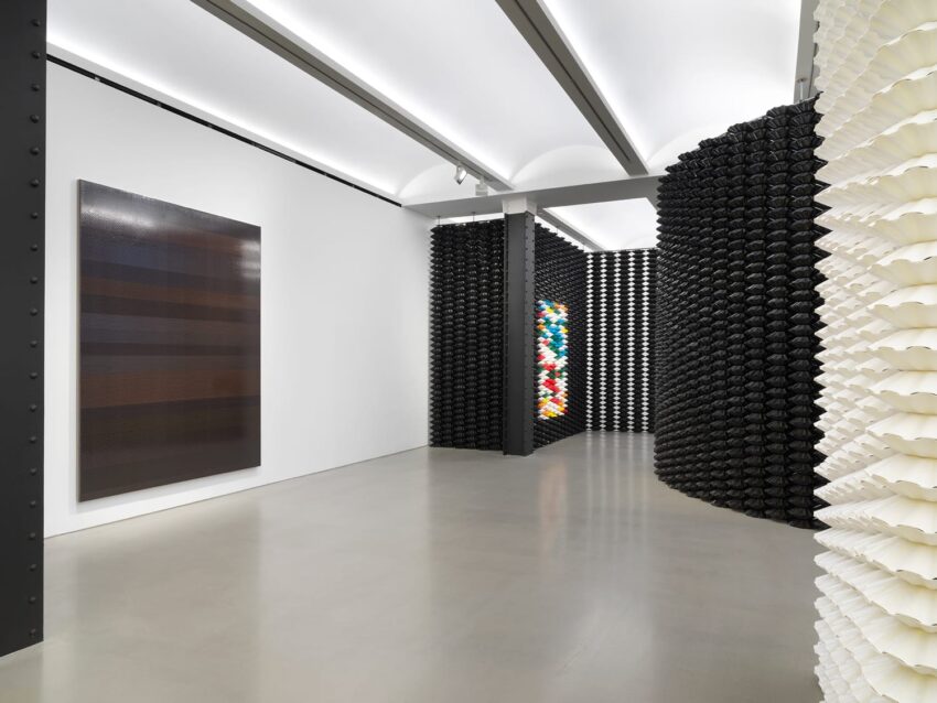 Contemporary art gallery with abstract paintings on walls and black and white textured installations on each side.