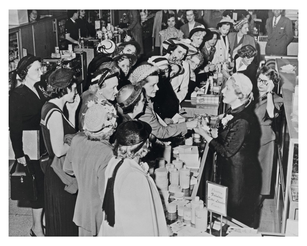 Women browsing and purchasing beauty products at a bustling cosmetic counter in a vintage department store setting.