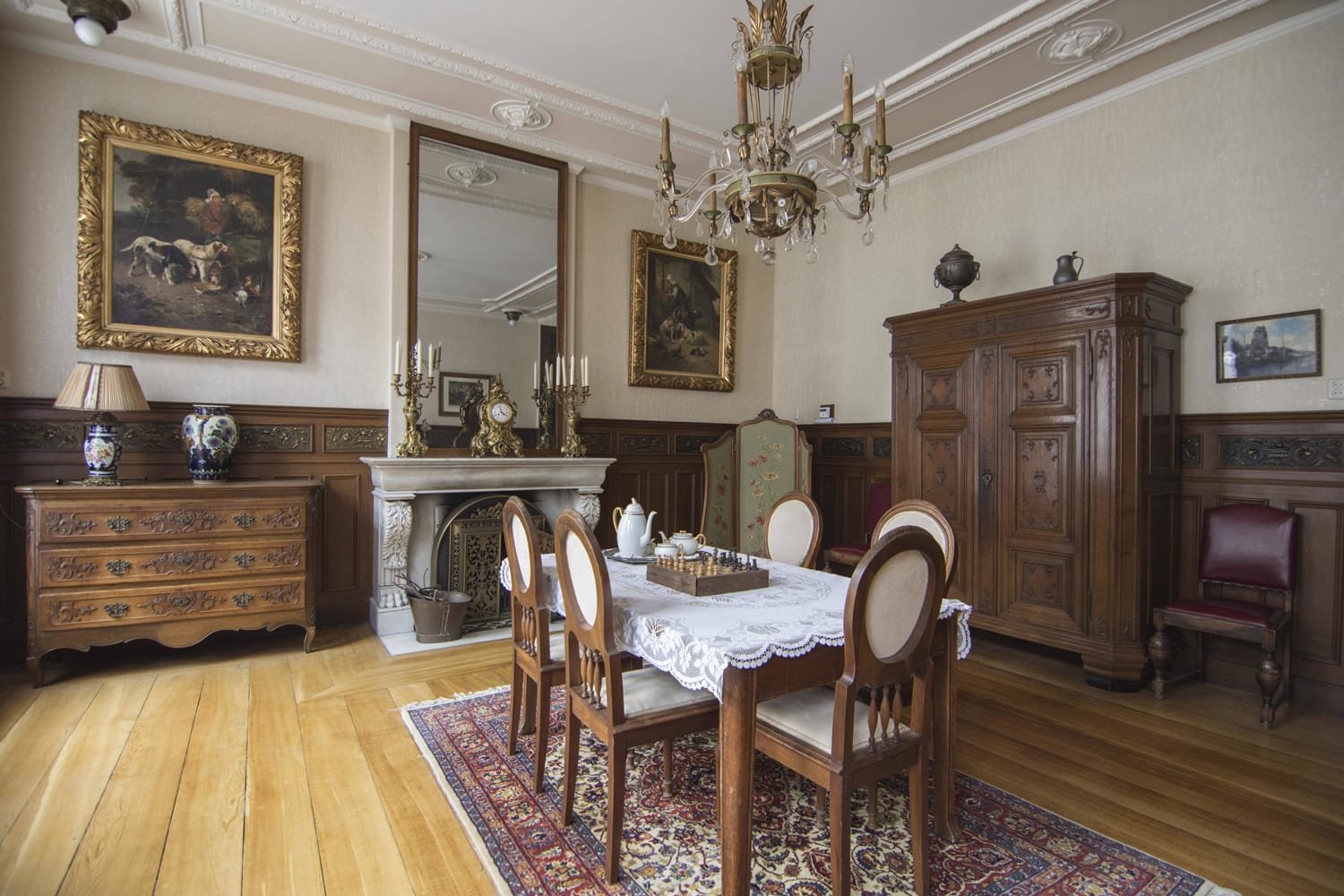 Victorian-style dining room with wooden furniture, ornate chandelier, vintage paintings, and a decorative fireplace.