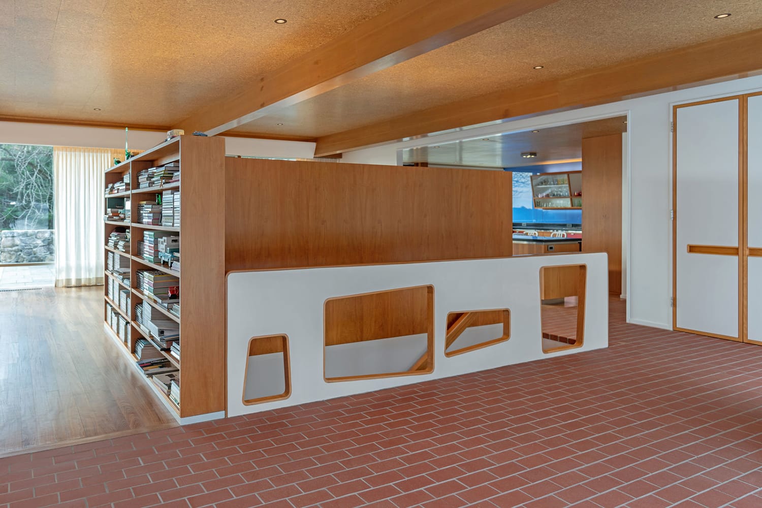 Interior of a modern room with wooden shelves, a unique white partition, and brick flooring.