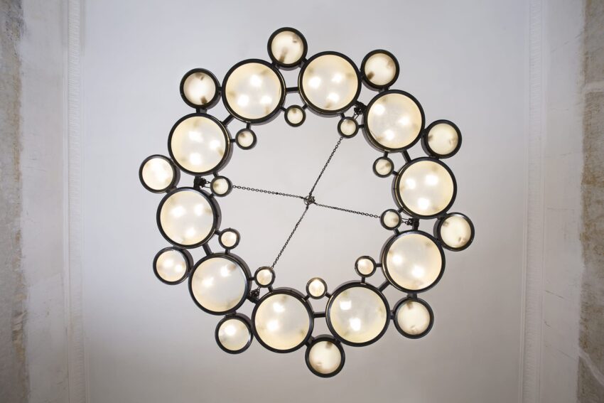 Modern circular chandelier with multiple illuminated globe lights viewed from below, set against a white ceiling.