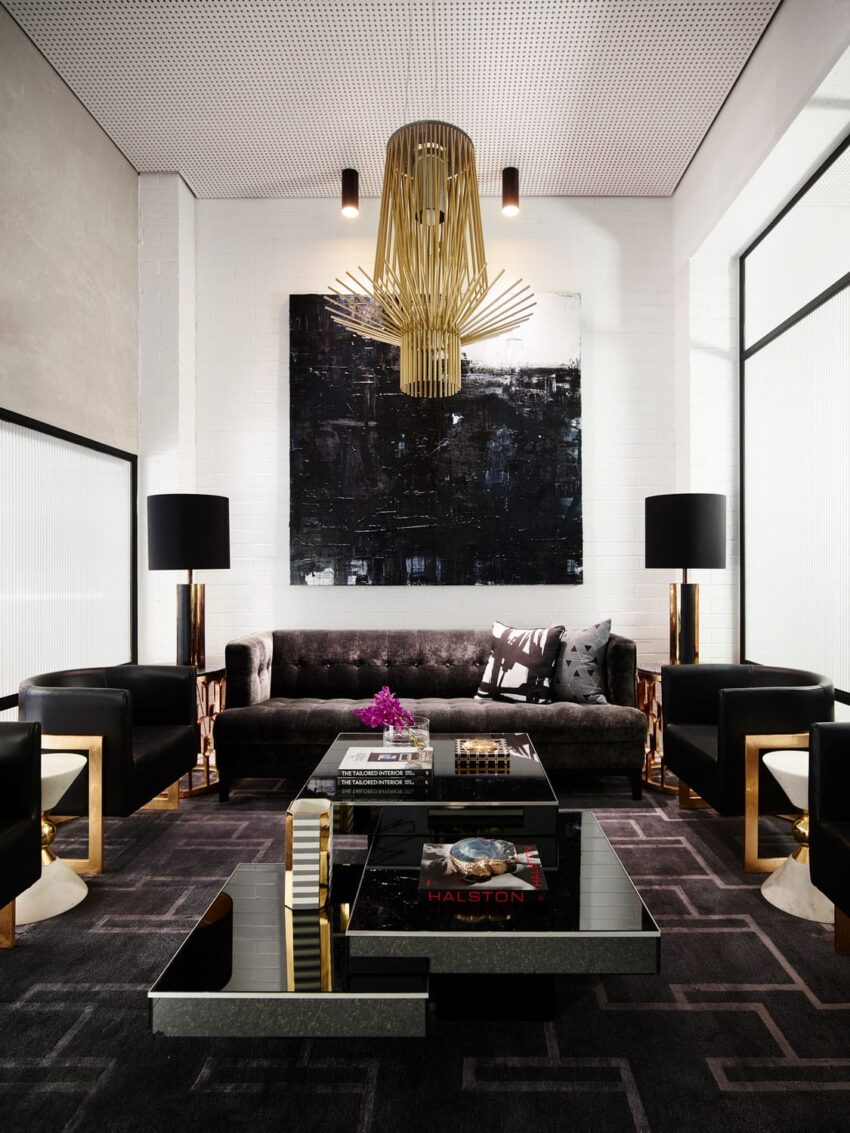 Modern living room with a gold chandelier, black sofa, abstract painting, coffee table, and two lamps on side tables.