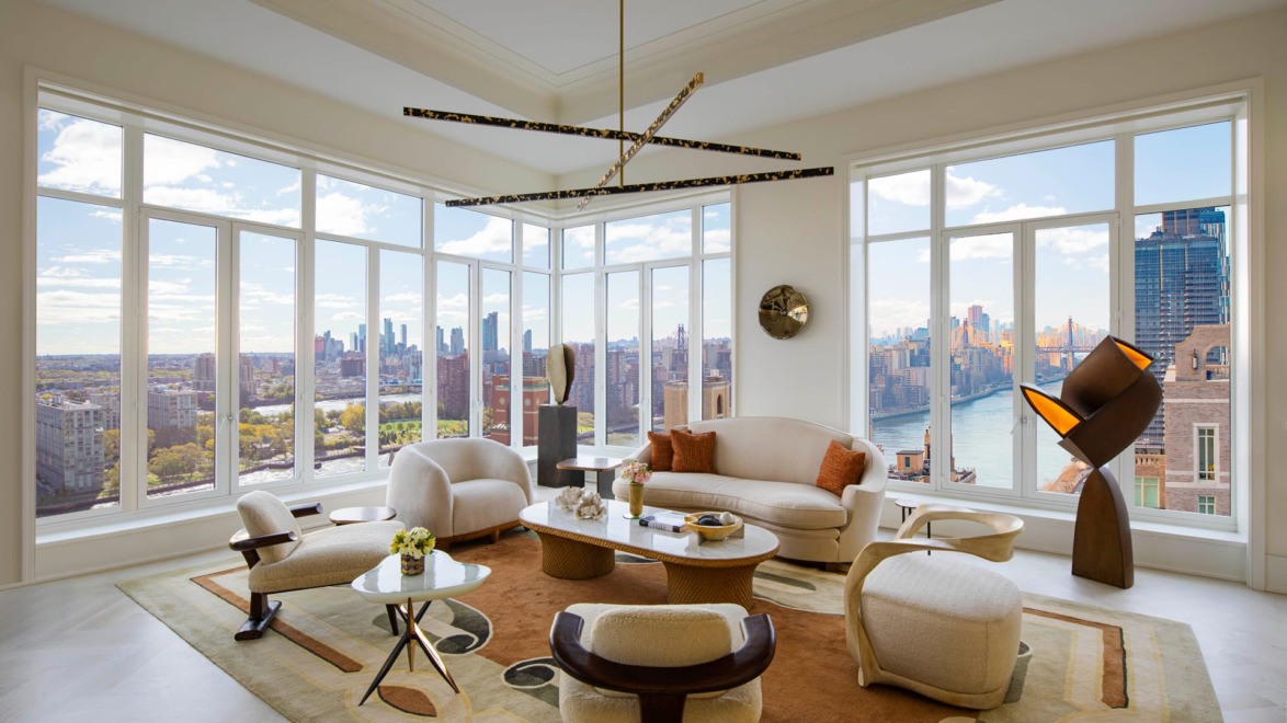 Modern living room with large windows, city skyline, and stylish furniture, including a round table and artistic lighting fixture.