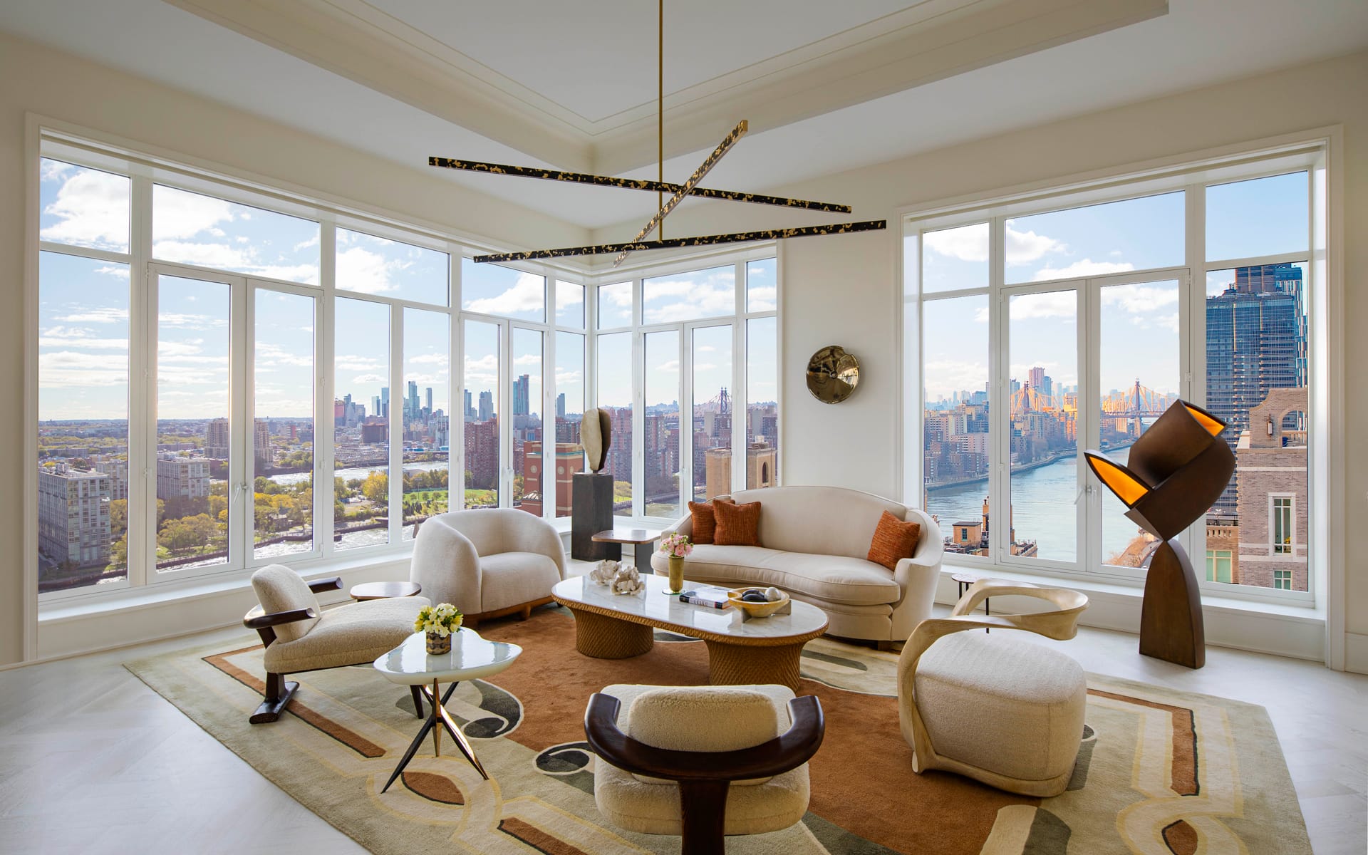Modern living room with large windows, city skyline, and stylish furniture, including a round table and artistic lighting fixture.