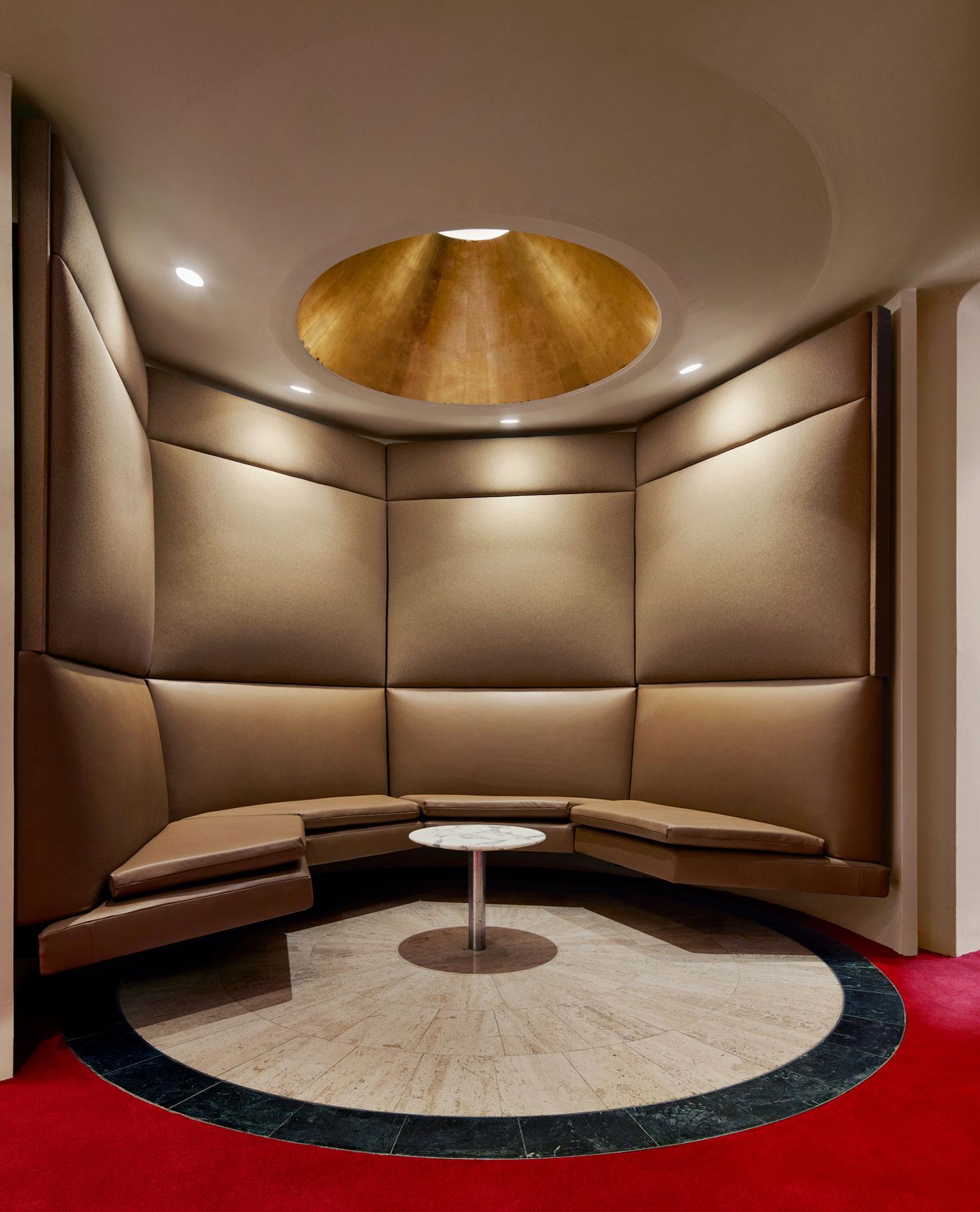 Modern circular seating area with padded walls, marble-topped table, and recessed lighting creating a cozy atmosphere.