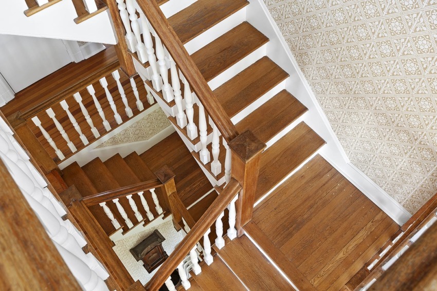 Top view of a multi-level wooden staircase with white railings and patterned wall, leading to a lower floor.