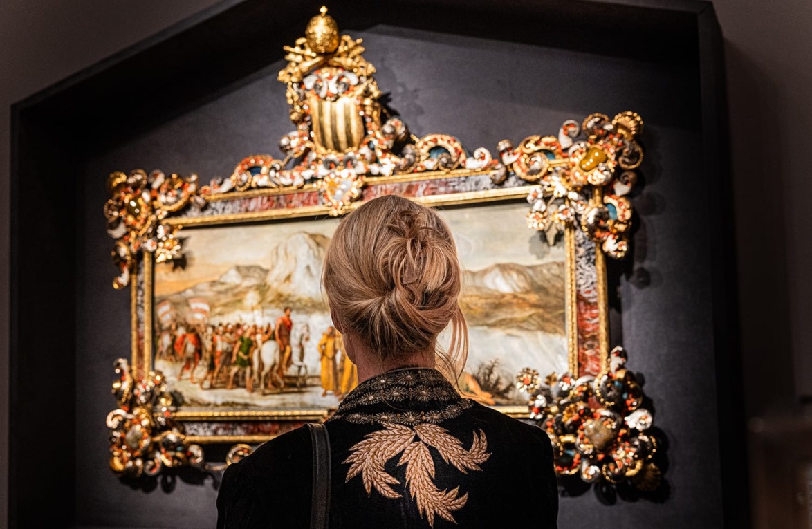 Person with blonde hair admiring ornate framed painting in a museum setting with intricate golden decorations.
