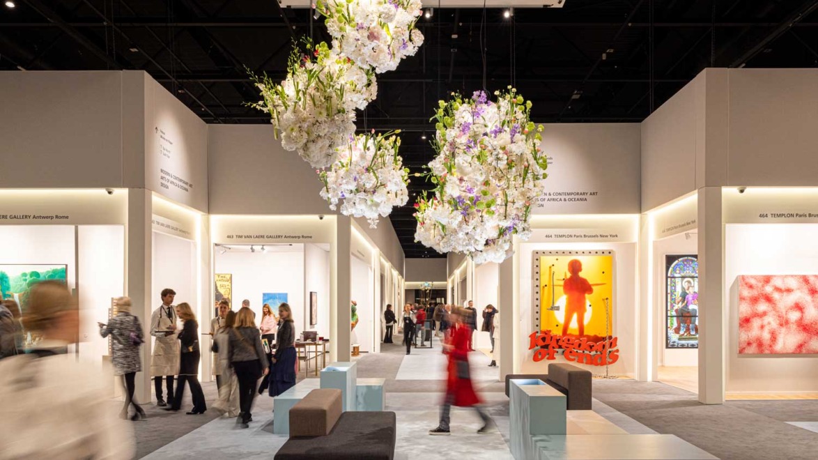 Art gallery with people viewing various colorful artworks and floral installations hanging from the ceiling.
