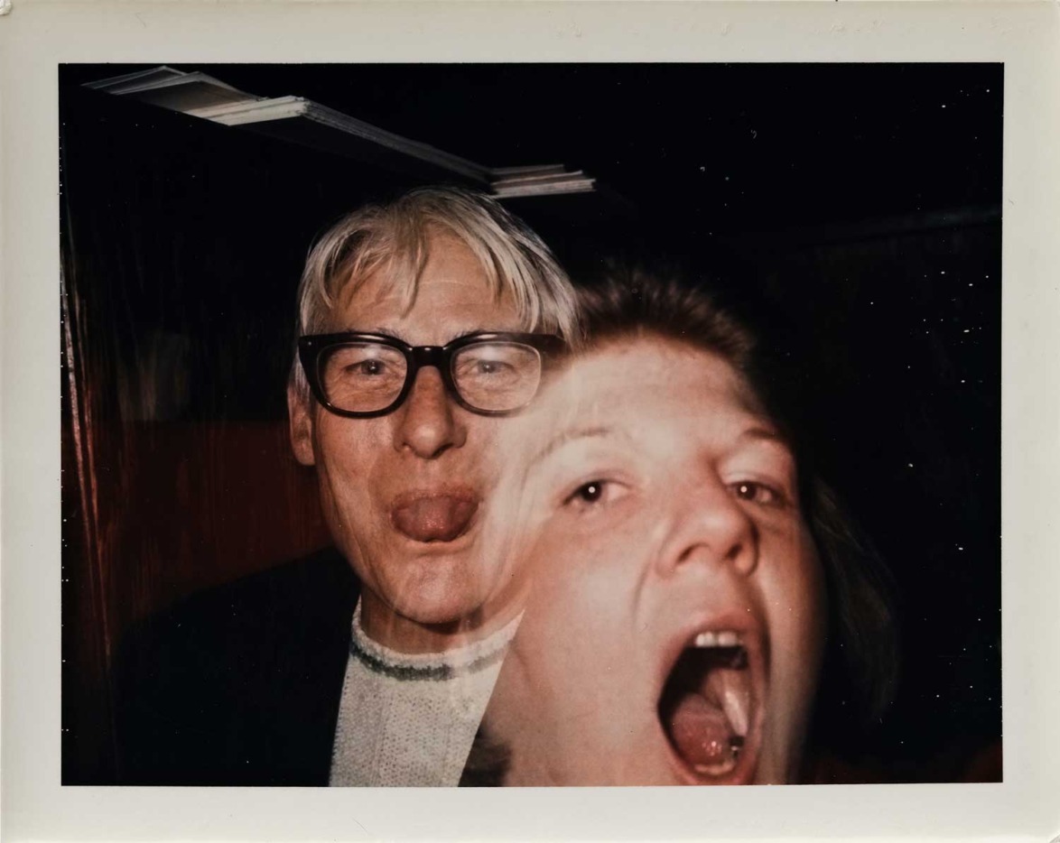 Two people making funny faces at the camera, one with glasses sticking out tongue, the other with mouth open wide.