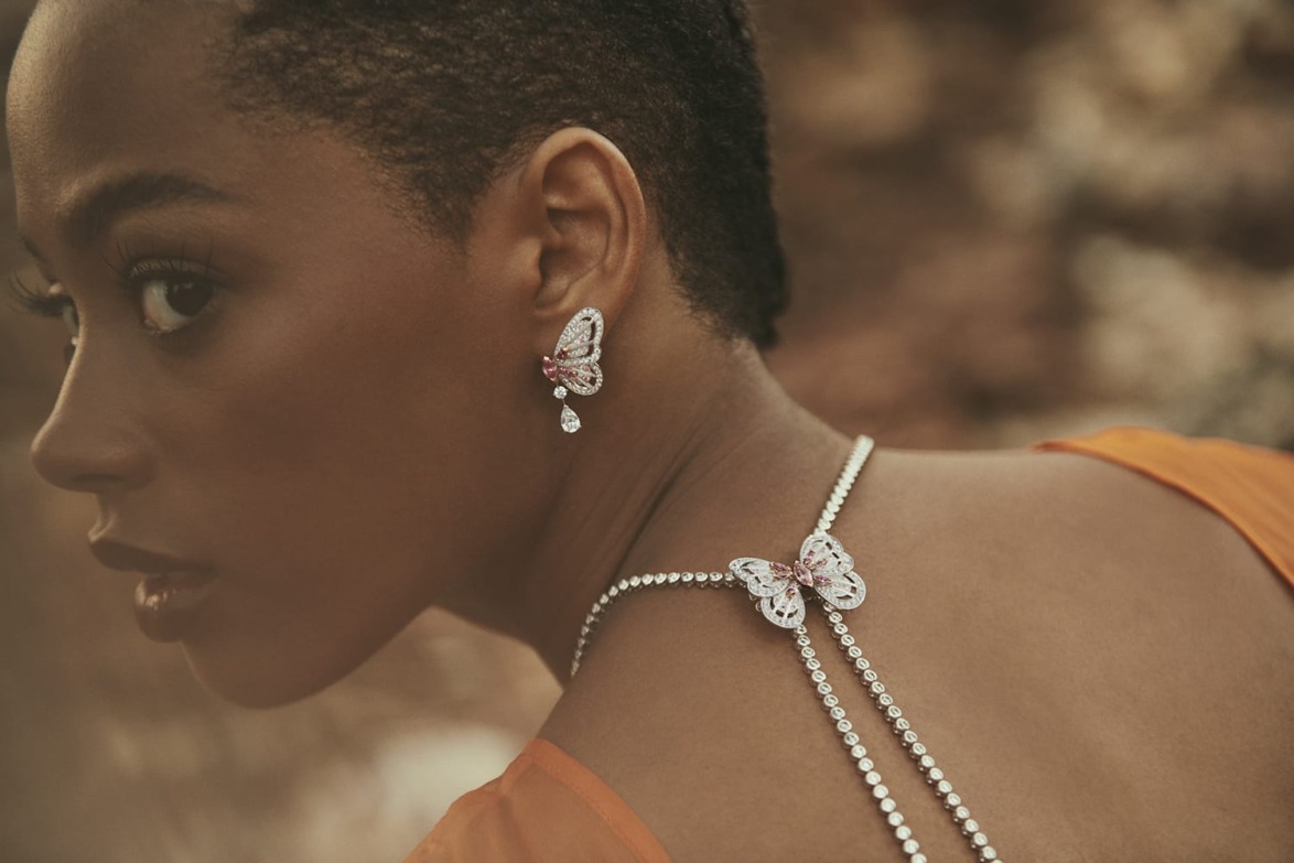 Woman in elegant orange dress wearing butterfly-themed jewelry with serene outdoor background.