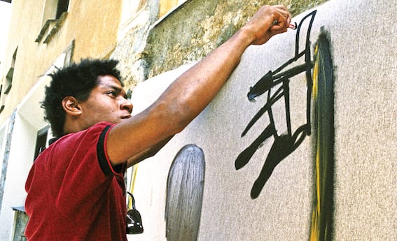 Person painting abstract art on a large canvas outdoors, wearing a red shirt.