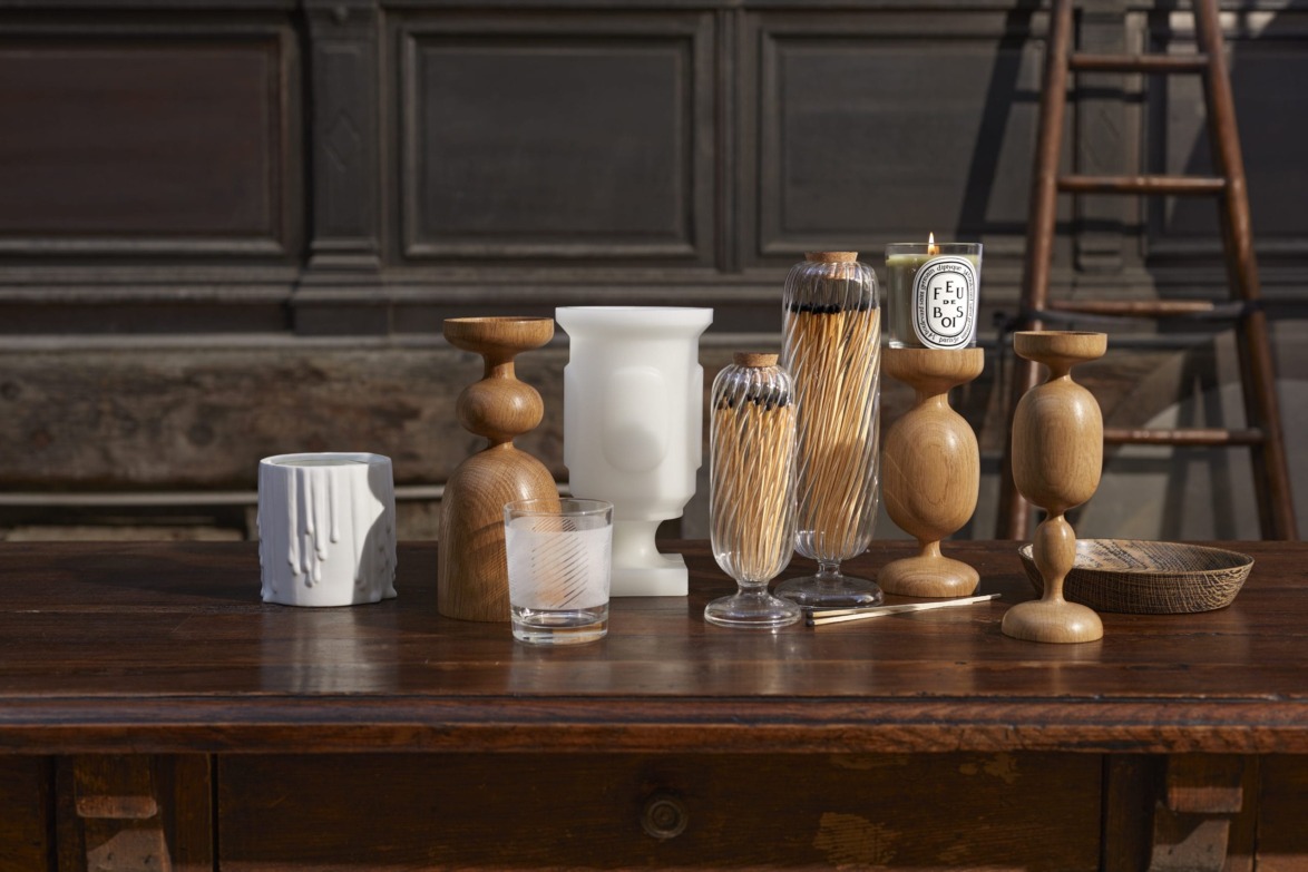 Wooden candle holders and glass vases arranged on a rustic wooden table with a ladder in the background.