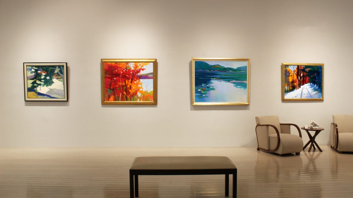 Art gallery with four colorful paintings on the wall and two chairs with a small table in the foreground.