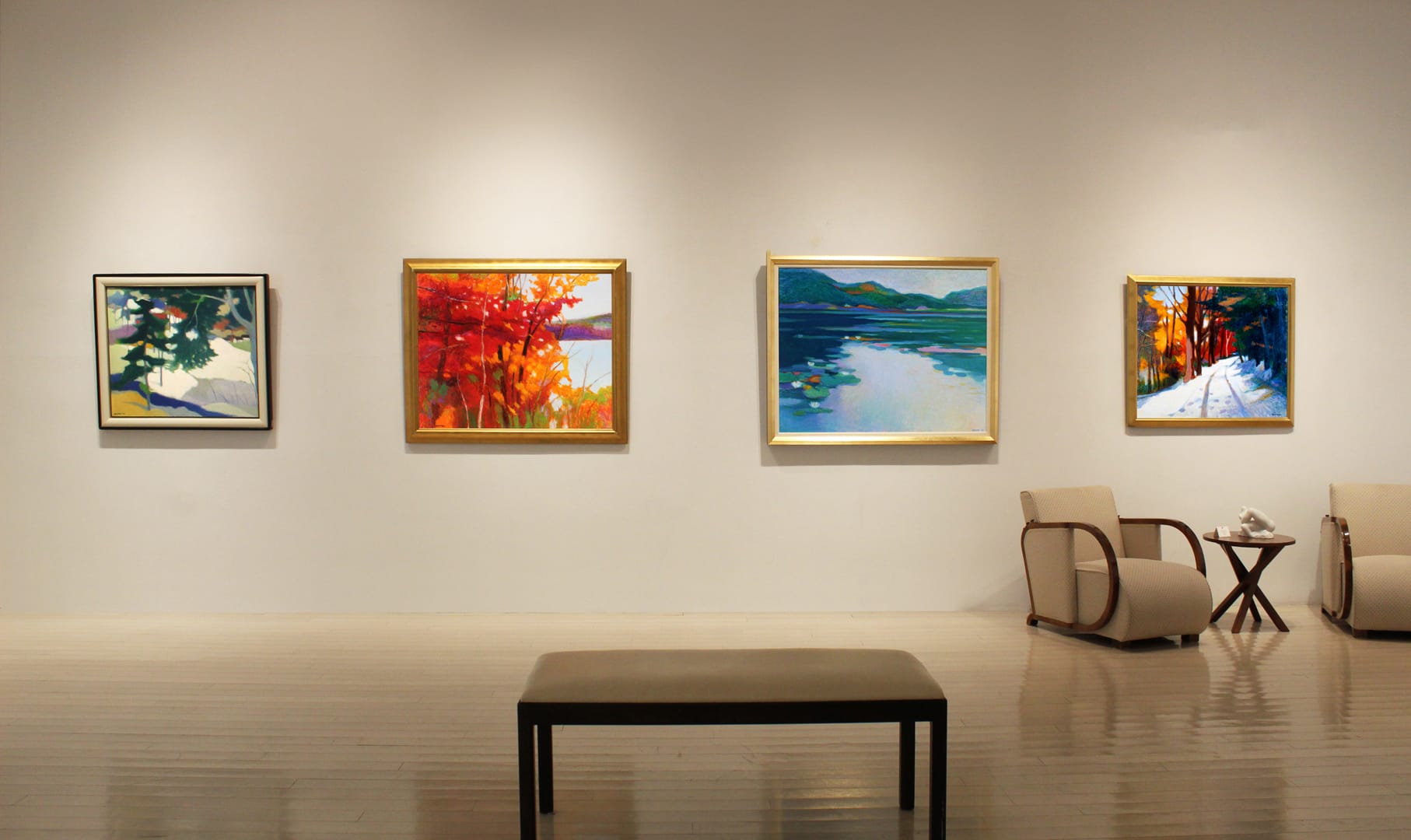 Art gallery with four colorful paintings on the wall and two chairs with a small table in the foreground.