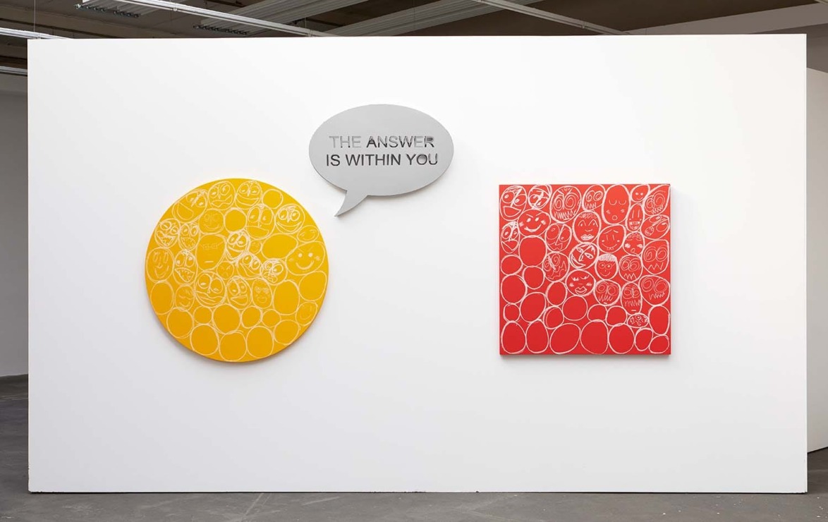 Art installation with an orange circle and a red square, with speech bubble saying "The answer is within you" on a white wall.