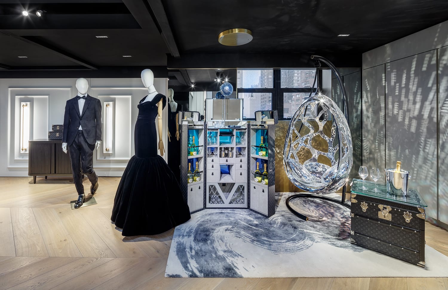 Elegant showroom with mannequins in formal wear, a crystal chair, modern cabinet, and luxury travel trunk in a stylish setting.