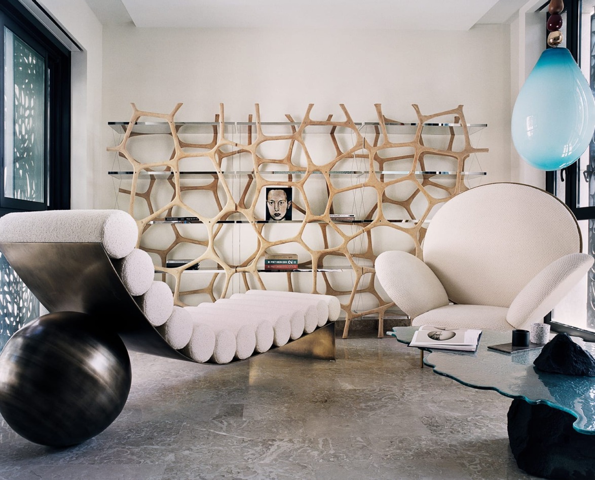 Modern living room with unique wooden shelf, abstract lounge chair, round armchair, turquoise glass table, and decorative items.