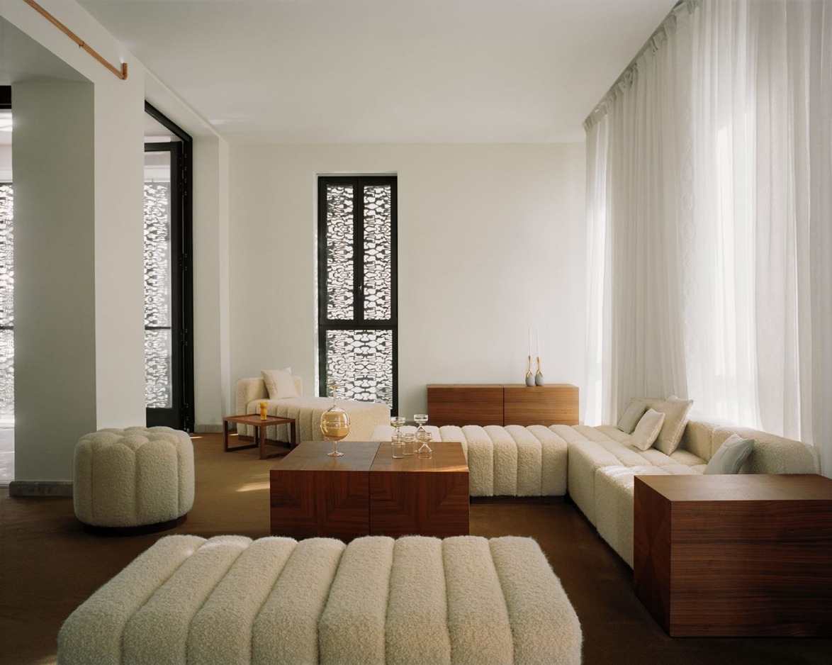 Modern living room with white sofas, wooden coffee tables, intricate window design, and soft natural light.