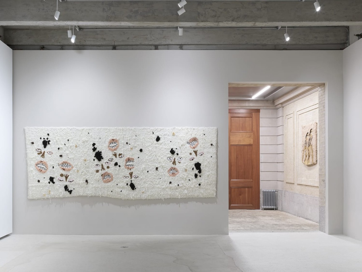 Gallery interior with contemporary textile art on white wall, featuring abstract floral patterns in a modern, minimalist setting.