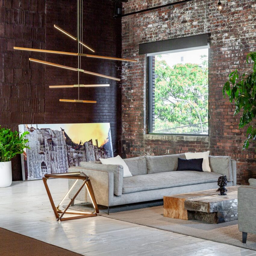 Modern loft interior with a gray sofa, unique lighting, green plants, and a large window with a view of greenery.