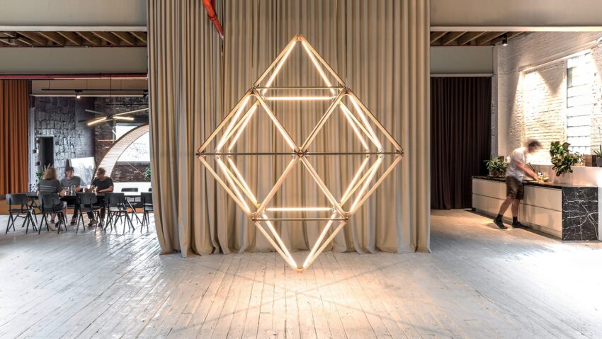 Geometric light sculpture in modern room with people sitting at a table and a person by the counter.